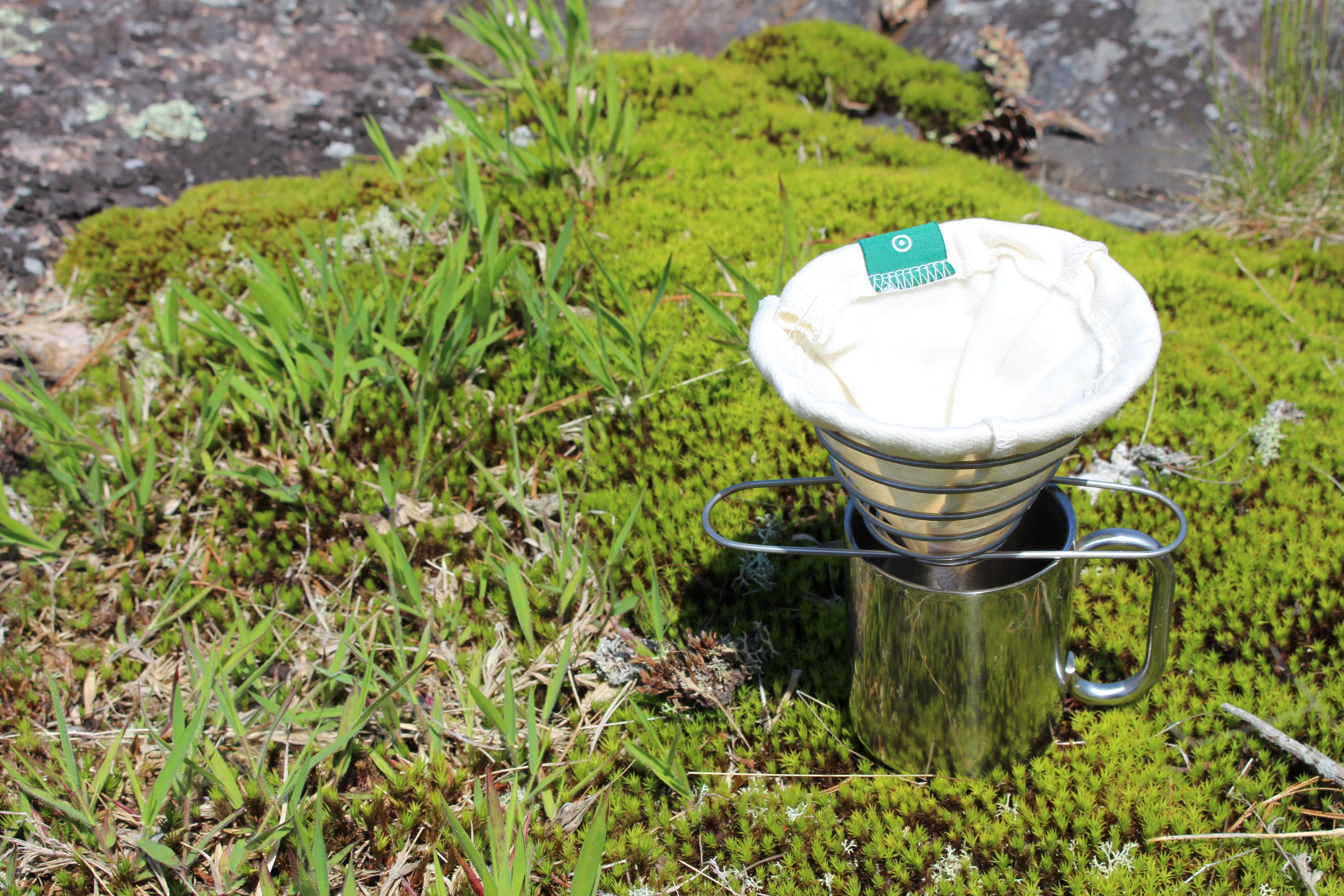 The ACE Brewer sitting on a stainless steel cup in moss while camping