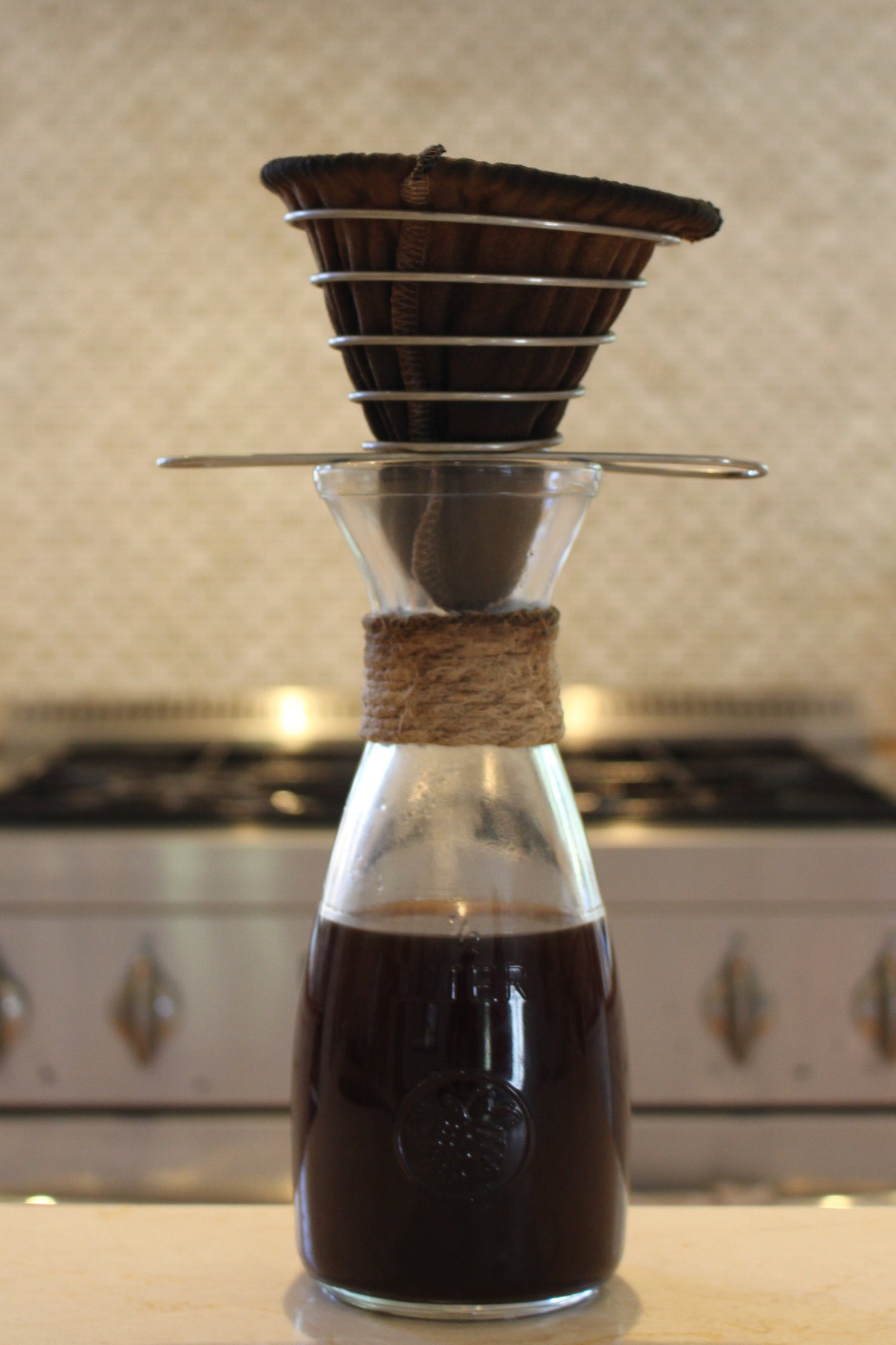 ACE Brewer with a darkly stained organic cotton filter set atop a glass carafe, demonstrating long-term use after nearly one year.